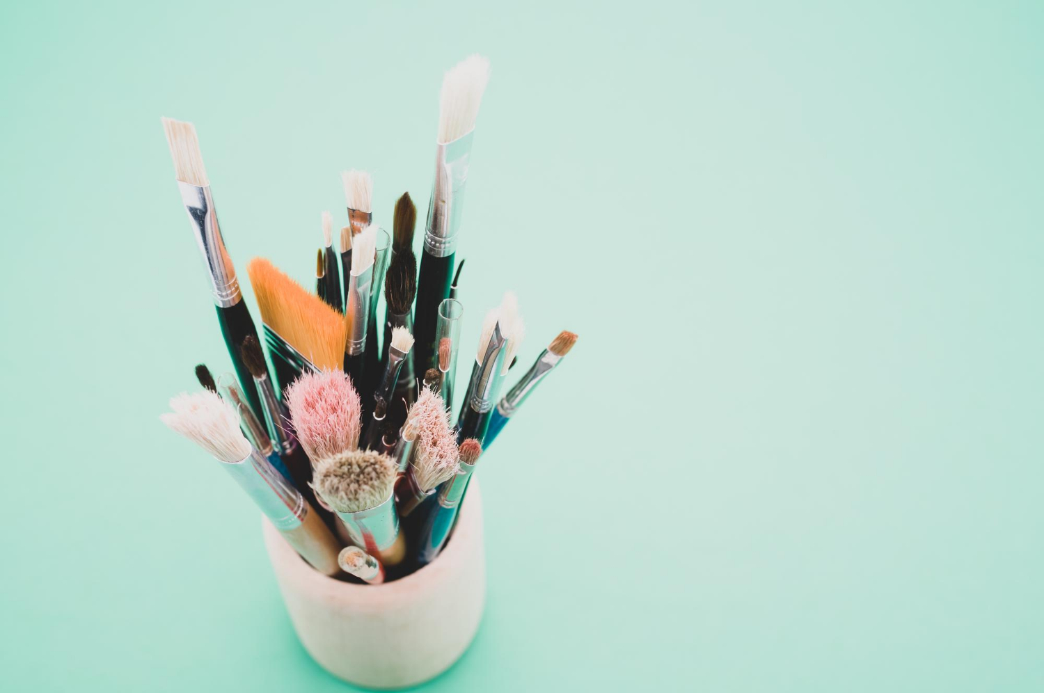 Closeup high-angle shot of paintbrushes in a cup placed on a green surface.