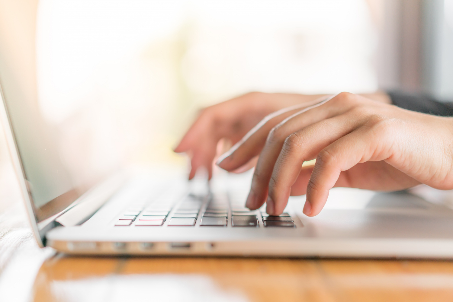 Closeup of a woman's hand typing on a laptop keyboard.