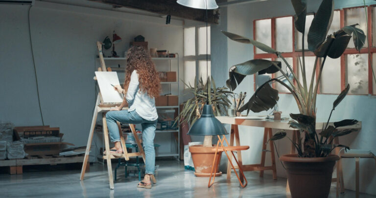 A long-haired female artist working on her canvas in an art studio.