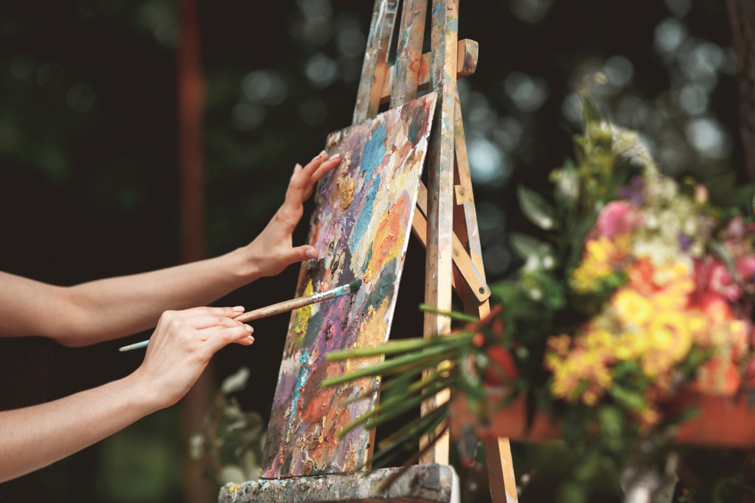 A closeup of an artist's hand painting on a small canvas.